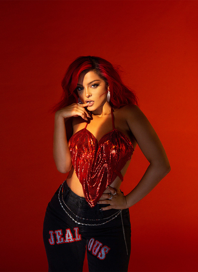 A picture of Bebe Rexha in front of a red background wearing a shiny red ne...